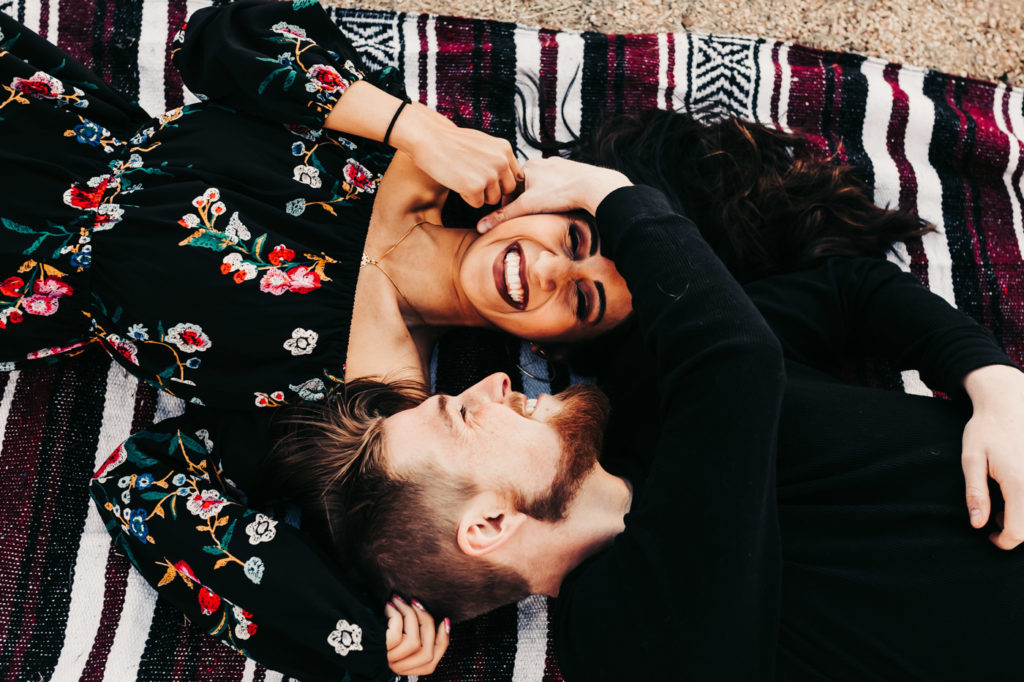 girl and boy laying on a blanked together laughing outside