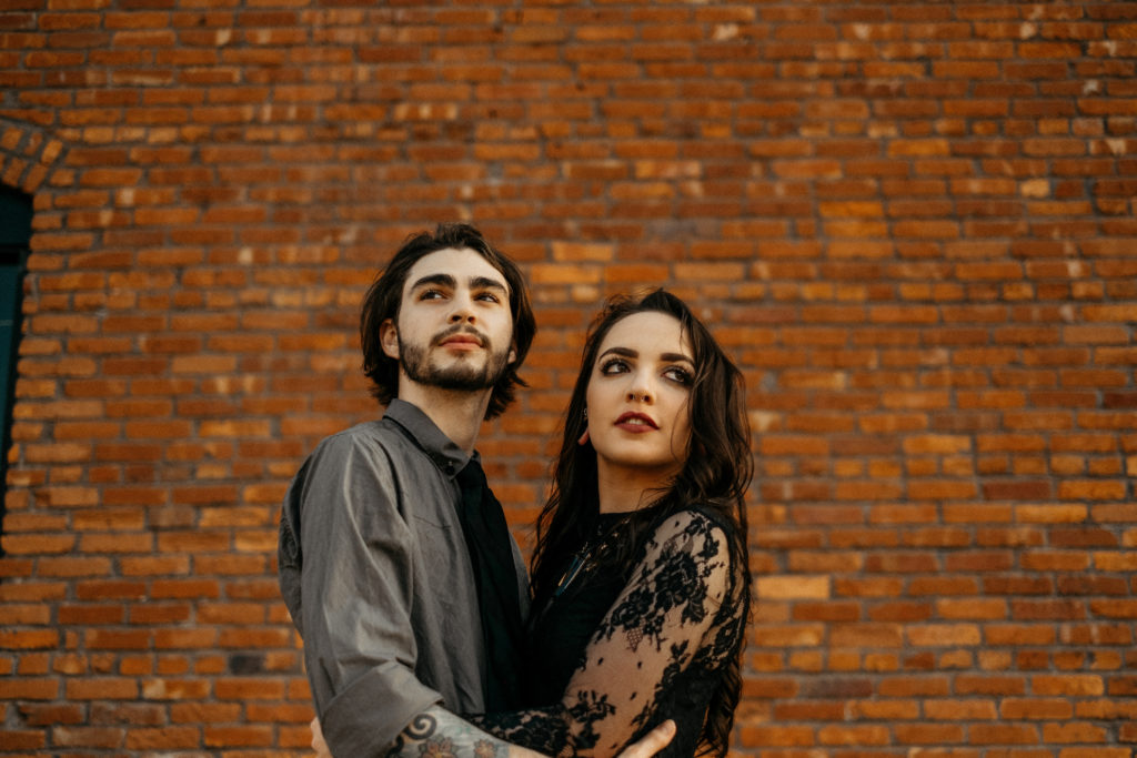 engaged couple looking in opposite directions in front of a brick wall