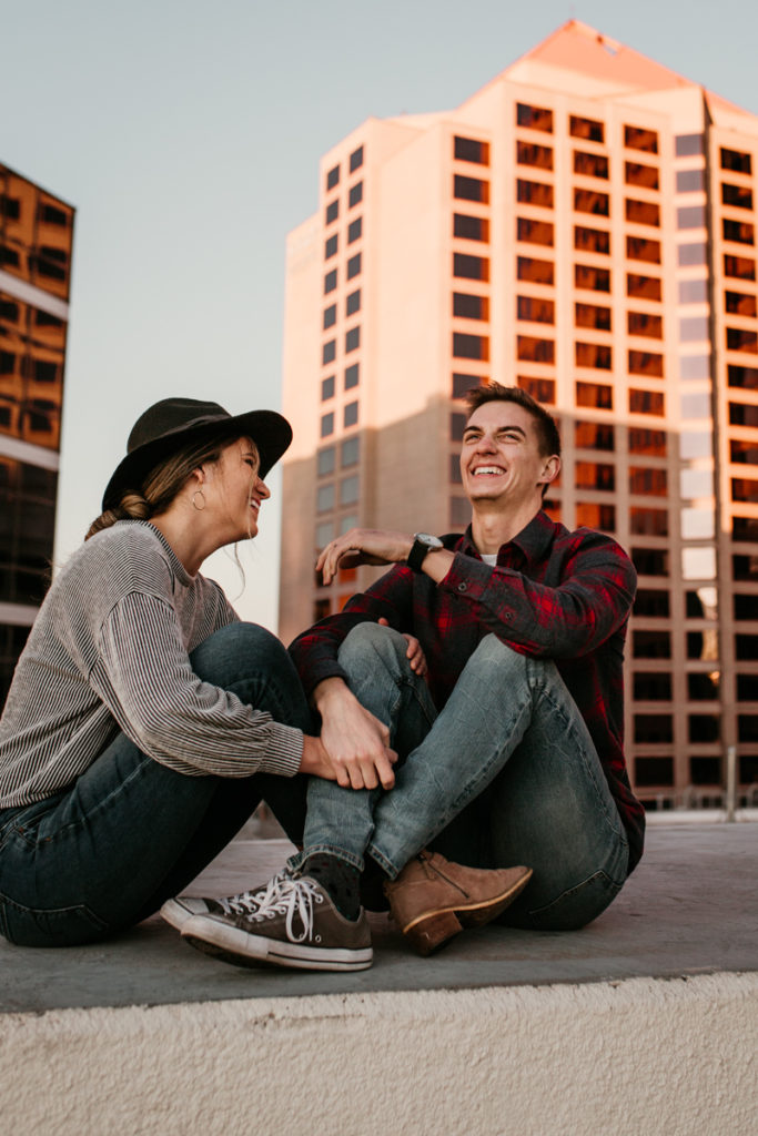 husband and wife sitting on top of a parking garage downtown laughing together