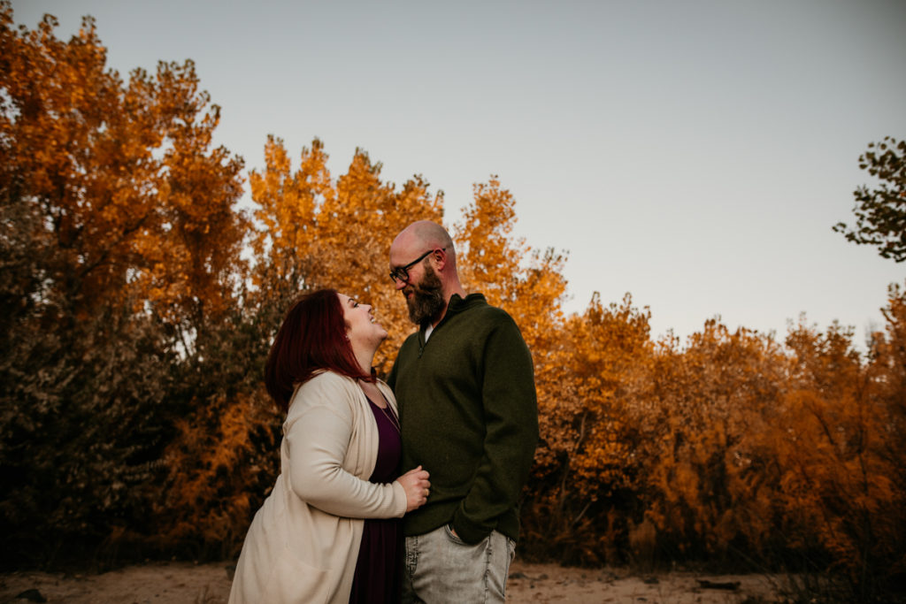 couple looking at each other in front of fall leaves 