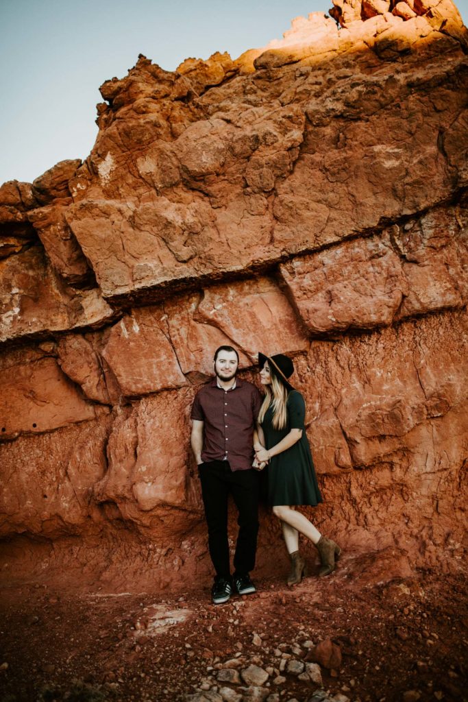 engaged couple leaning against red rocks