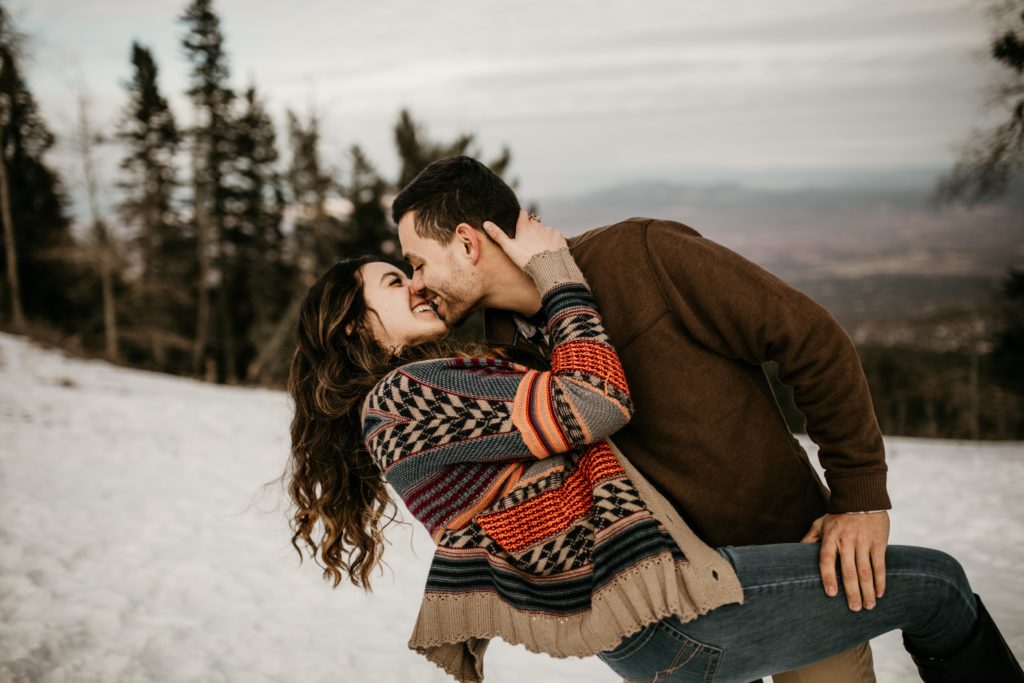 boyfriend and girlfriend about to kiss in the snow on top of a mountain