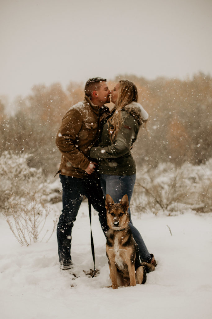 Couple kissing in the snow with their dog