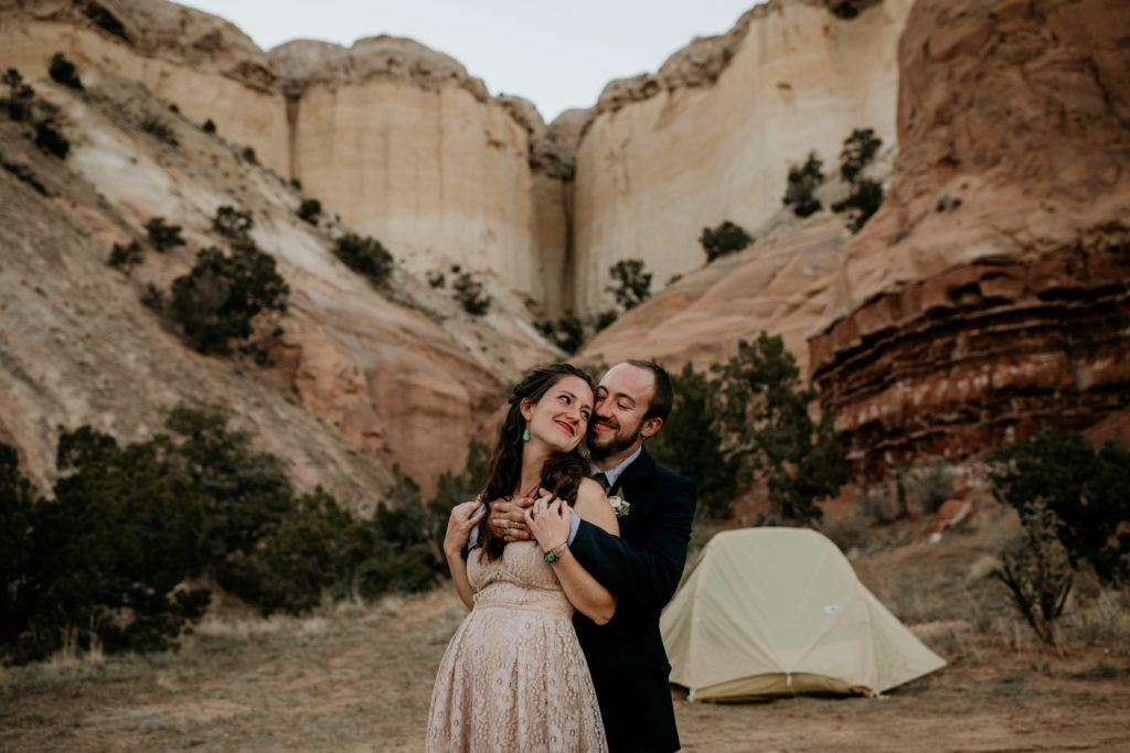 bride and groom kissing in front of a red rock canyon at a campsite