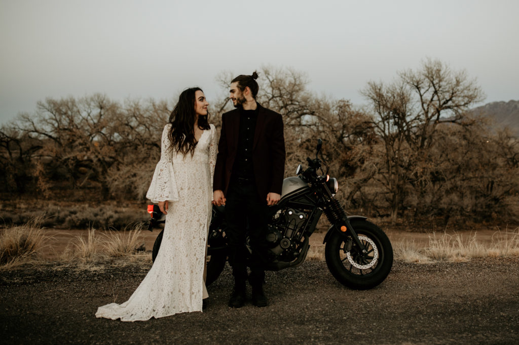 bride and groom standing in front of a motorcycle