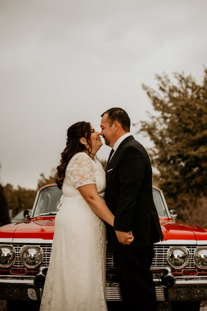 husband and wife standing in front of a classic Cadilac together in wedding clothes