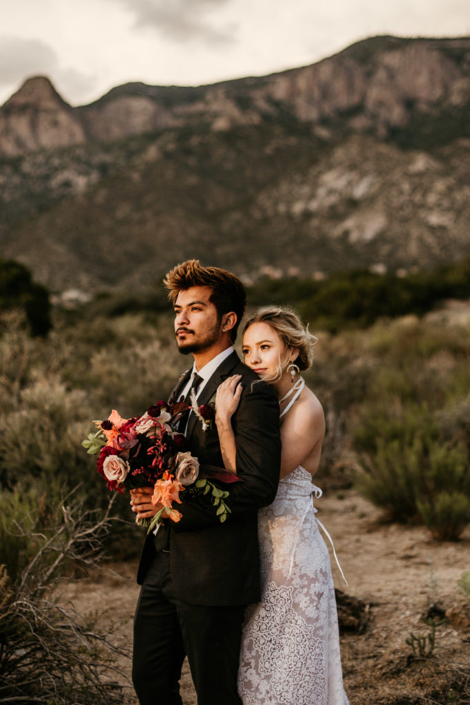 bride holding groom from behind in front of the sandia mountain foothills