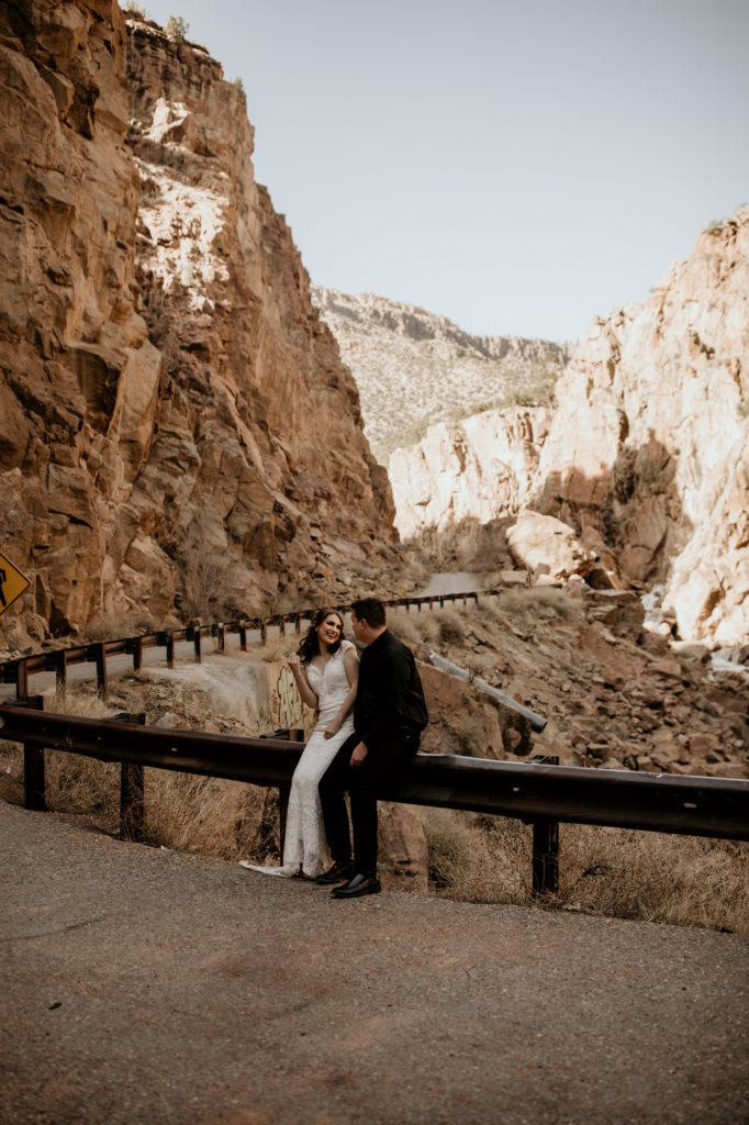 bride and groom sitting on a guard rail next to a canyon