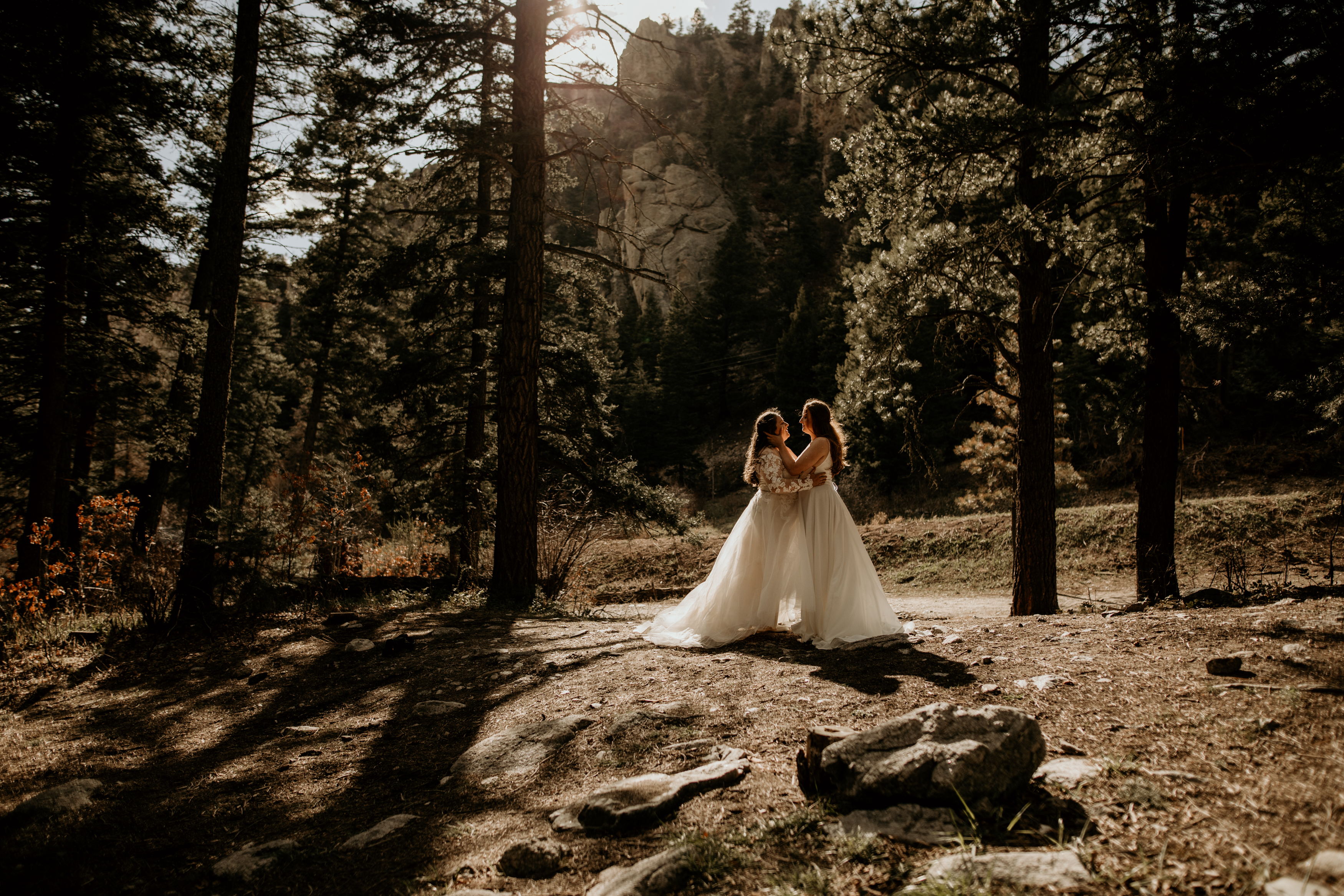 same sex couple standing in a forest about to kiss wearing their wedding gowns