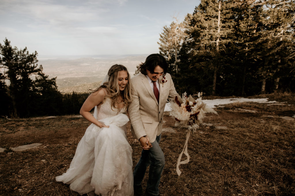 bride and groom running together on top of a mountain