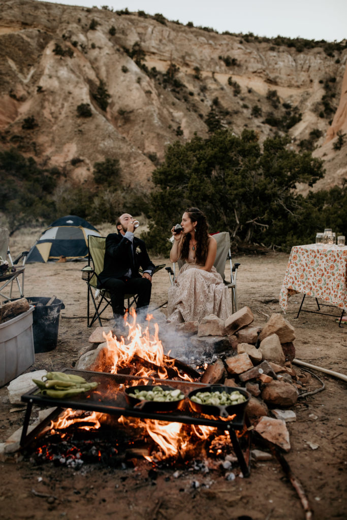 husband and wife sitting at their campsite together in wedding clothes