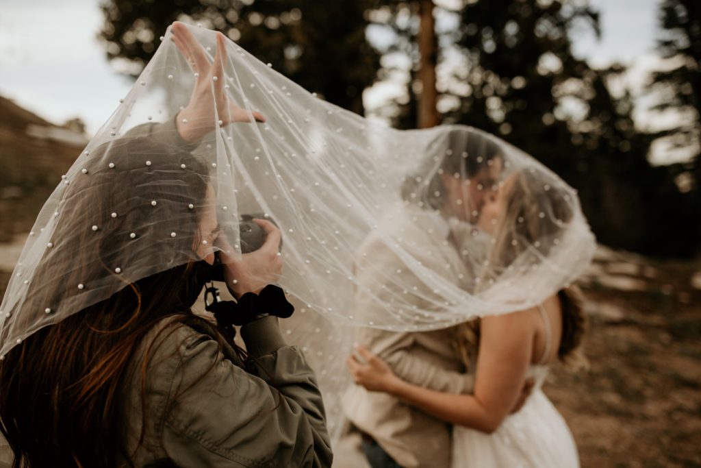 photographer taking photos of a bride and groom kissing under a veil