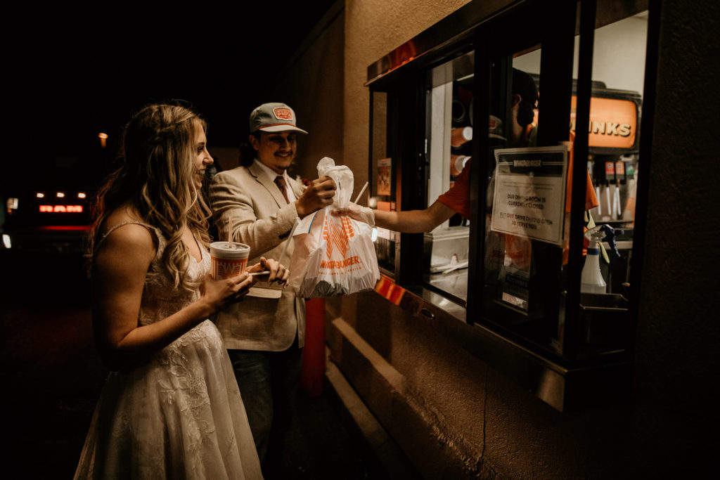 husband and wife grabbinge food at a drive thru window in wedding clothes