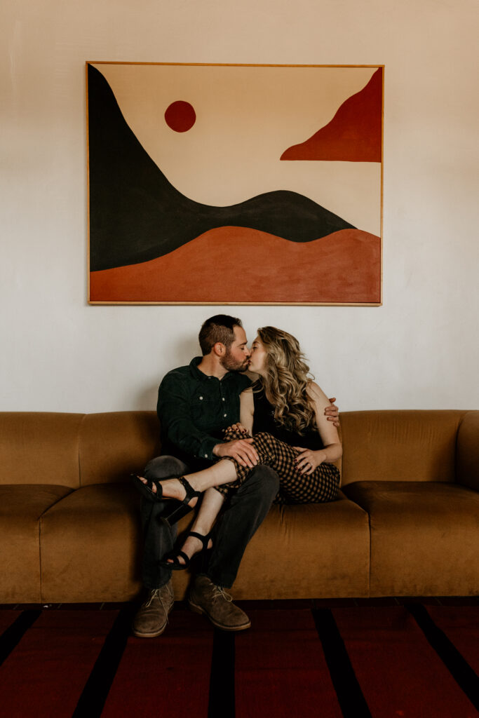 Engaged couple sitting on a retro couch together kissing. 